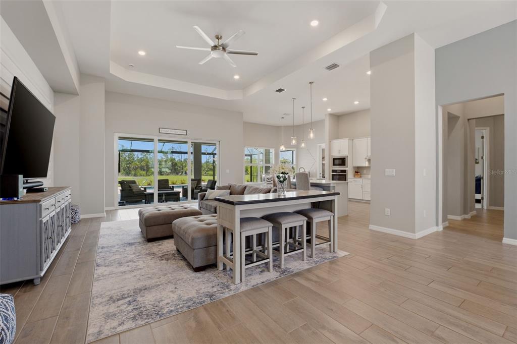 An open-concept living room features a tray ceiling, tile flooring, and a view of a pool — 12299 WELLEN GOLF STREET, VENICE, FL