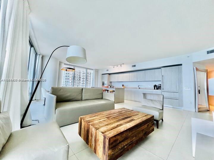 A modern living room features a large wooden coffee table, a sofa, and an open kitchen — 4111 S Ocean Dr # 1801, Hollywood FL 33019, HOLLYWOOD, FL