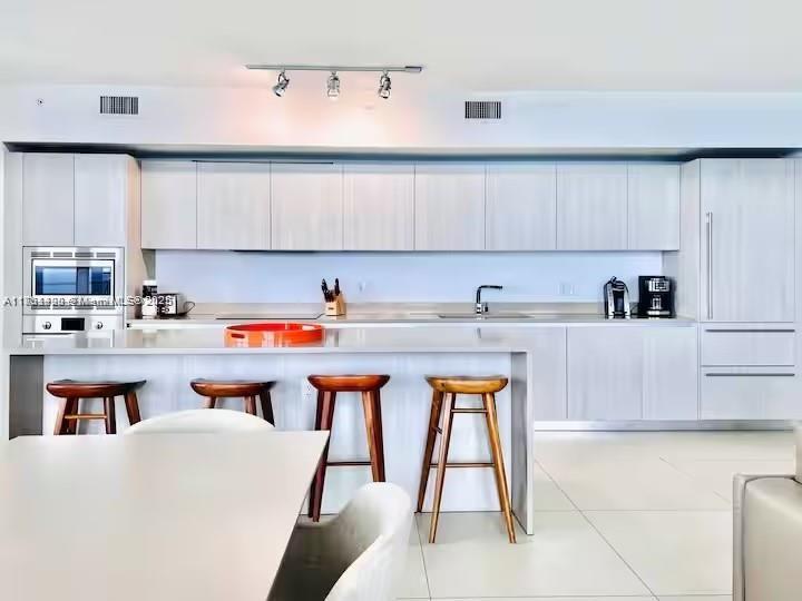 A modern kitchen features light wood cabinetry, a central island with bar stools, and stainless appliances — 4111 S Ocean Dr # 1801, Hollywood FL 33019, HOLLYWOOD, FL
