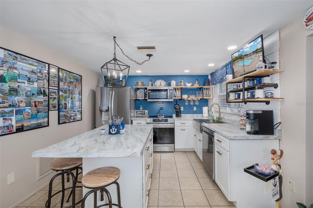 A kitchen features white cabinets, a marble-topped island, blue walls, and industrial-style shelving — 8225 SAN FELIPE COURT, PORT RICHEY, FL