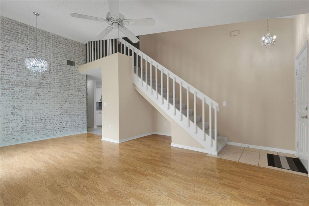 A living room features a white brick accent wall, a staircase, and light wood flooring — 1084 MEADOWOOD POINTE ROAD, LAKELAND, FL
