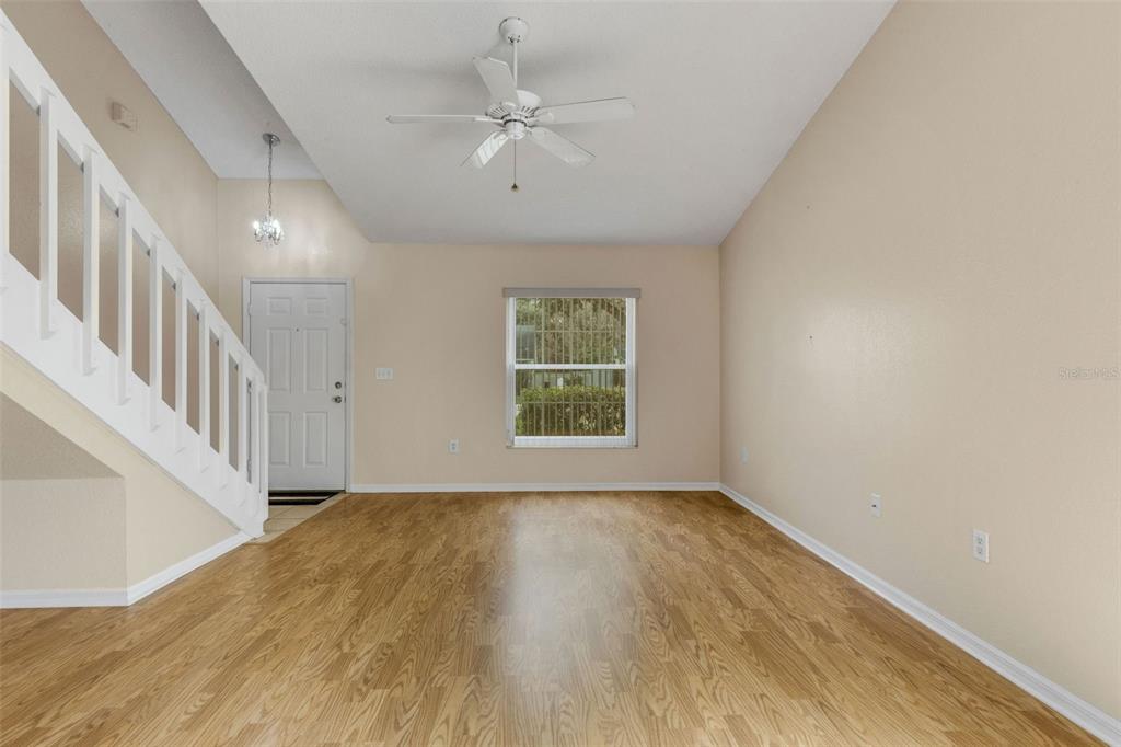 An empty living room features light wood-look flooring, a white staircase, and a ceiling fan — 1084 MEADOWOOD POINTE ROAD, LAKELAND, FL