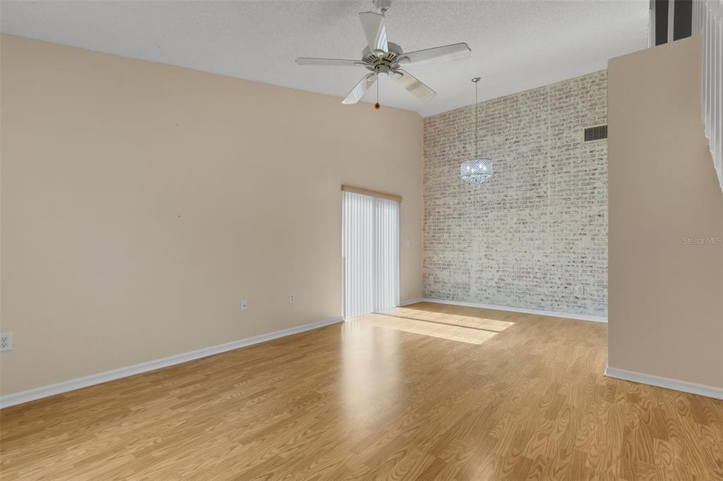 A living room features light wood flooring, a vaulted ceiling, and a white brick accent wall — 1084 MEADOWOOD POINTE ROAD, LAKELAND, FL