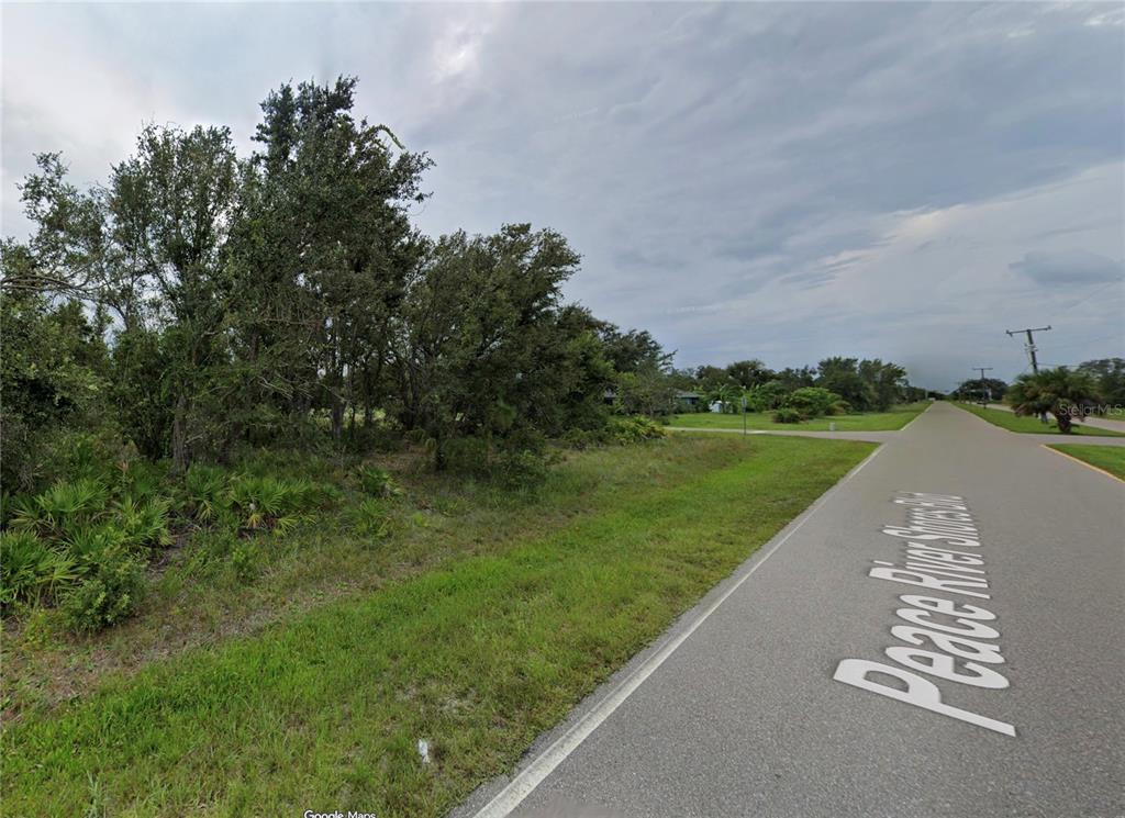 A paved road runs alongside a vacant, tree-covered lot under a cloudy sky — 29411 PEACE RIVER SHORES BOULEVARD, PUNTA GORDA, FL