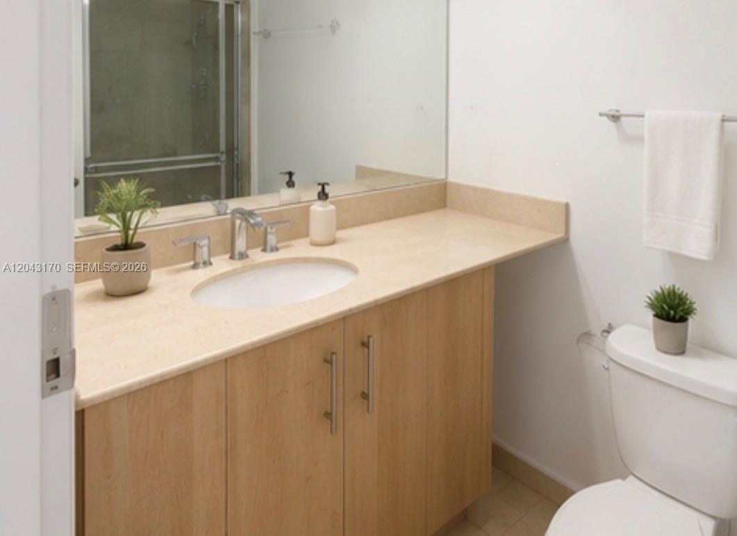 A bathroom features a light wood vanity, a beige countertop, and a wall-mounted mirror — 10275 Collins Ave # 115, Bal Harbour FL 33154, BAL HARBOUR, FL
