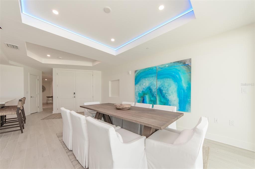A dining room features a wooden table, white slipcovered chairs, and a blue abstract painting — 15 AVALON STREET UNIT 702, CLEARWATER BEACH, FL