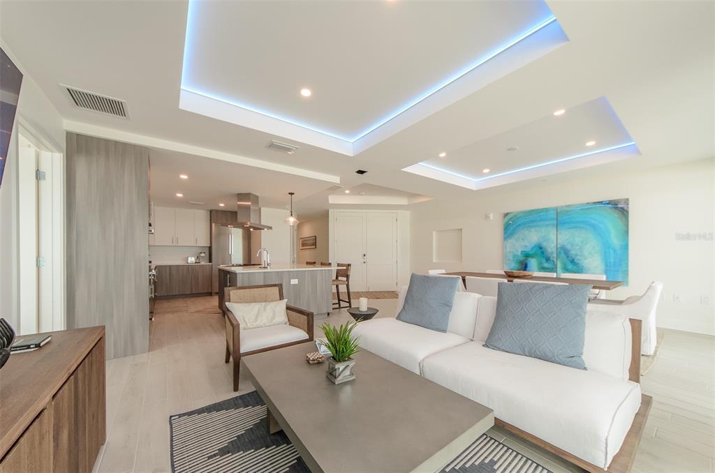 An open-concept living and dining area features recessed tray ceilings with blue LED accent lighting — 15 AVALON STREET UNIT 702, CLEARWATER BEACH, FL