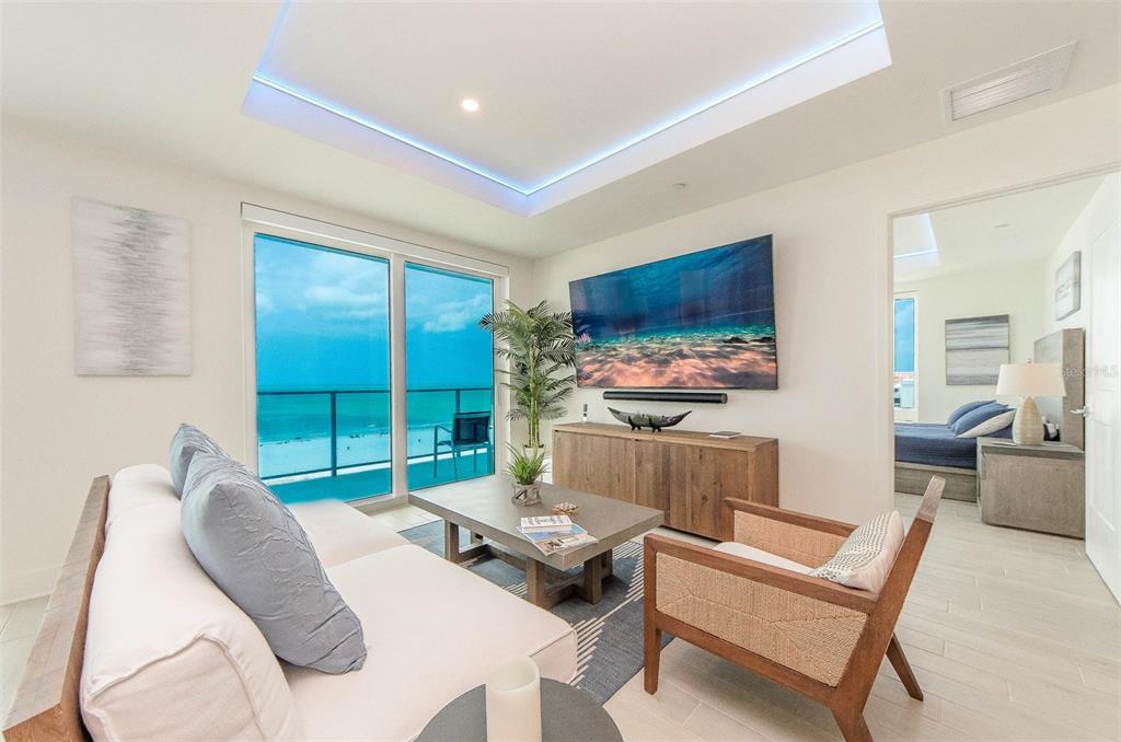 A living room with a large television, wooden console, and sliding doors overlooking the ocean — 15 AVALON STREET UNIT 702, CLEARWATER BEACH, FL