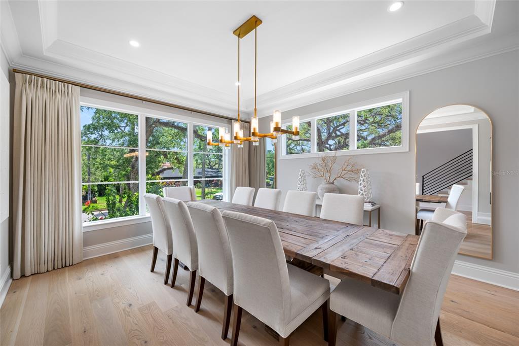 A dining room features a long wooden table, upholstered chairs, a gold chandelier, and windows — 2623 S PARKVIEW STREET, TAMPA, FL