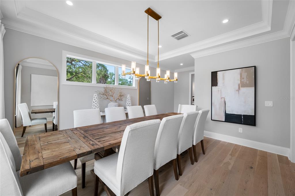 A dining room features a long wooden table, upholstered chairs, and a modern gold chandelier — 2623 S PARKVIEW STREET, TAMPA, FL