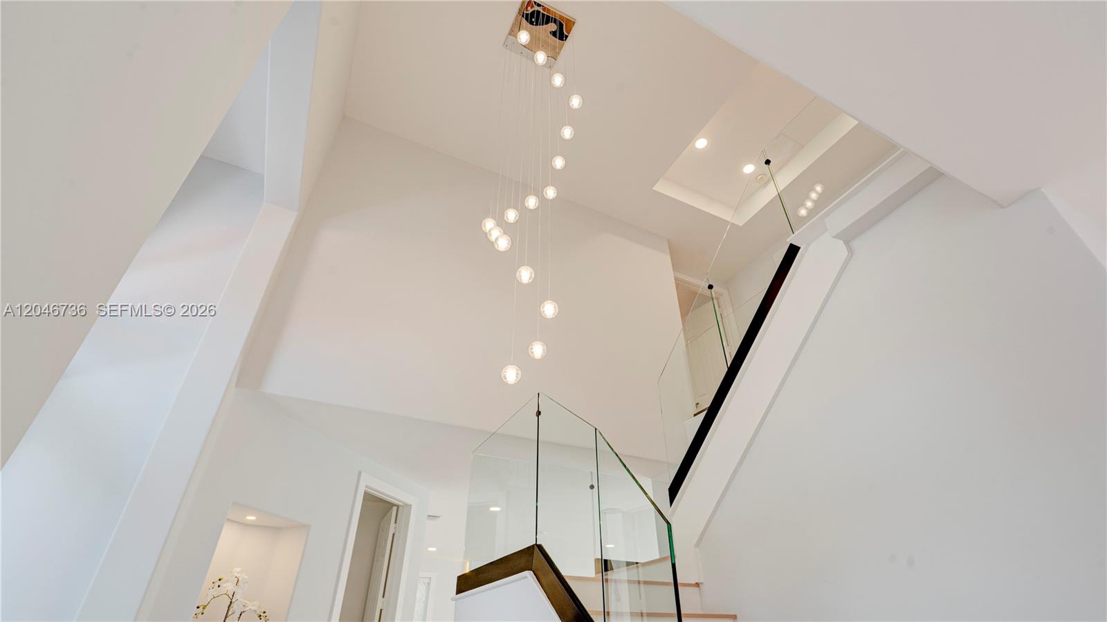 A modern staircase with glass railings sits beneath a tall ceiling and hanging light fixture — 7956 SW 195th St, Cutler Bay FL 33157, CUTLER BAY, FL