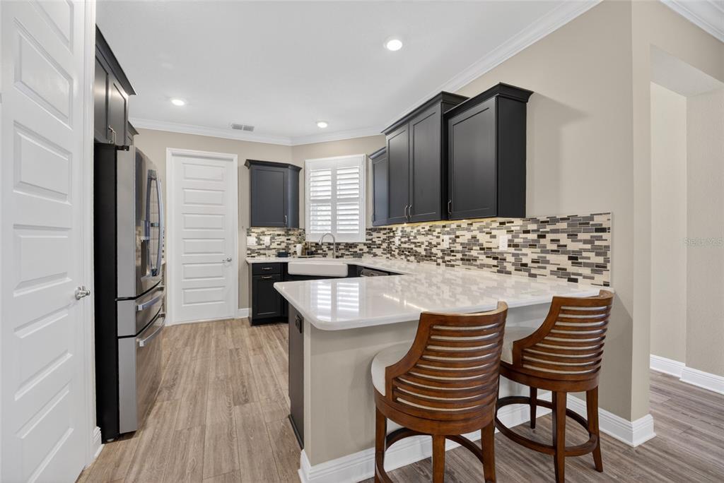 A kitchen features dark cabinets, a white farmhouse sink, quartz countertops, and two wooden barstools — 10363 SW 96TH LOOP, OCALA, FL