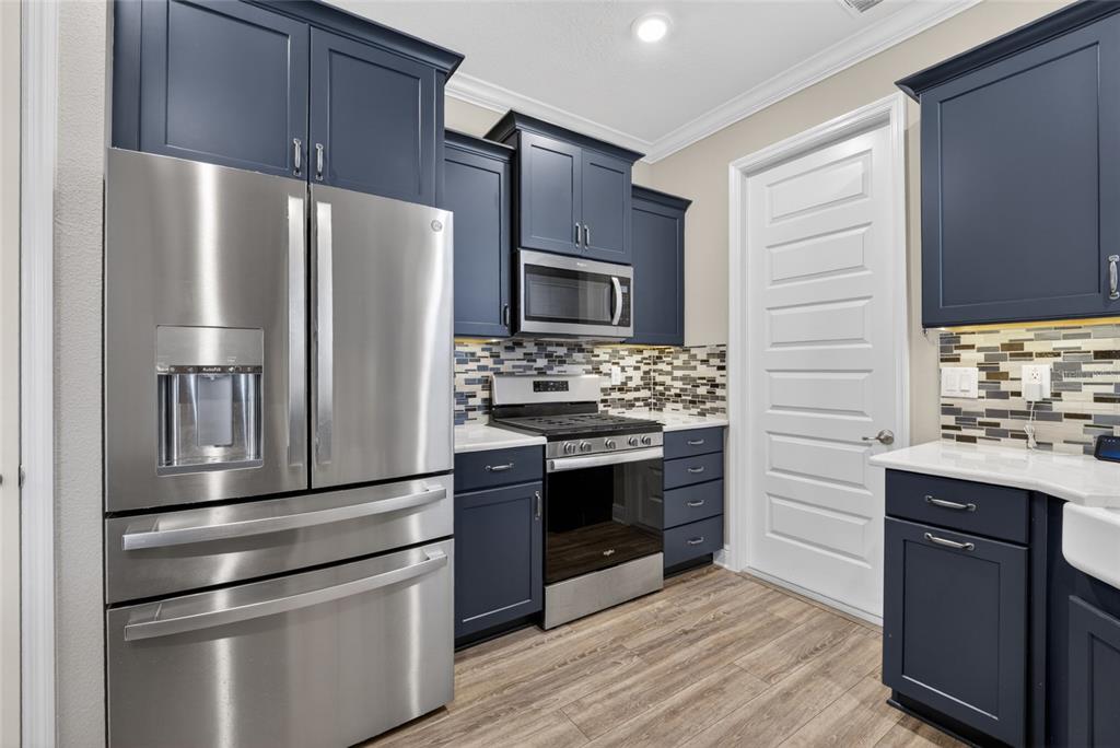 A kitchen features dark blue cabinets, stainless steel appliances, and a mosaic tile backsplash — 10363 SW 96TH LOOP, OCALA, FL