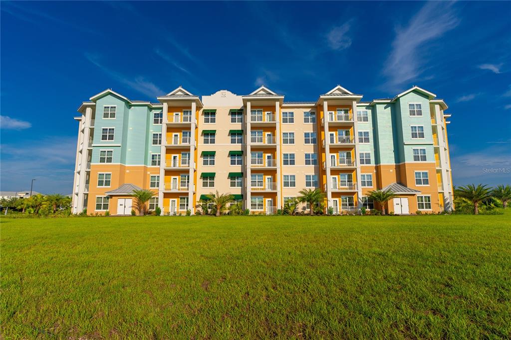 A multi-story apartment building with a colorful facade stands behind a large grassy lawn — 8061 VACATION AVENUE UNIT 309, KISSIMMEE, FL