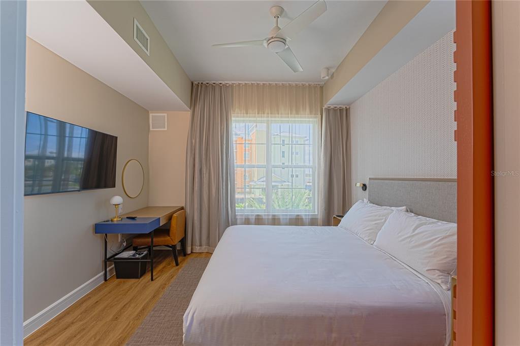 A bedroom features a king bed, a blue desk, a wall-mounted television, and a window — 8061 VACATION AVENUE UNIT 309, KISSIMMEE, FL