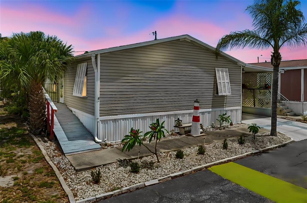 A single-story mobile home with gray siding, a wheelchair ramp, and a decorative lighthouse statue — 12701 126TH AVENUE UNIT 63, LARGO, FL