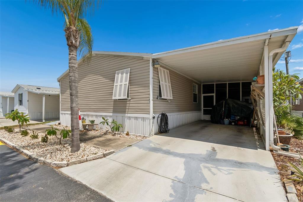 A tan mobile home features a concrete driveway, a covered carport, and a palm tree — 12701 126TH AVENUE UNIT 63, LARGO, FL