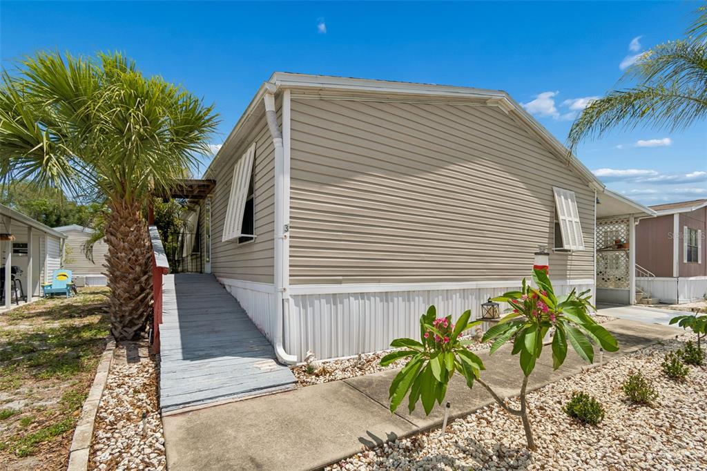 A beige mobile home features a wooden ramp, white shutters, and a palm tree outside — 12701 126TH AVENUE UNIT 63, LARGO, FL