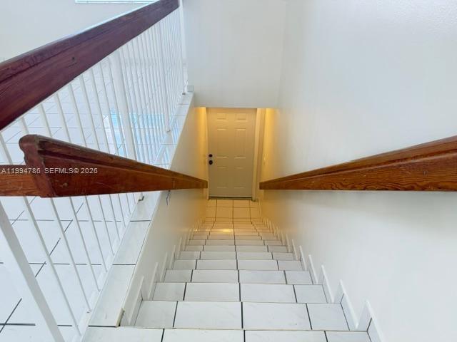 A staircase with white tiled steps and wooden handrails leads down to a closed door — 3260 W 70th St # 202, Hialeah FL 33018, HIALEAH, FL