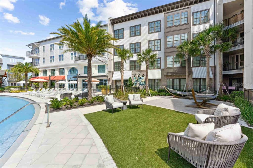 A swimming pool area features lounge chairs, palm trees, and outdoor seating on a lawn — 1464 LAUREL SOUND LANE UNIT B5, SANFORD, FL