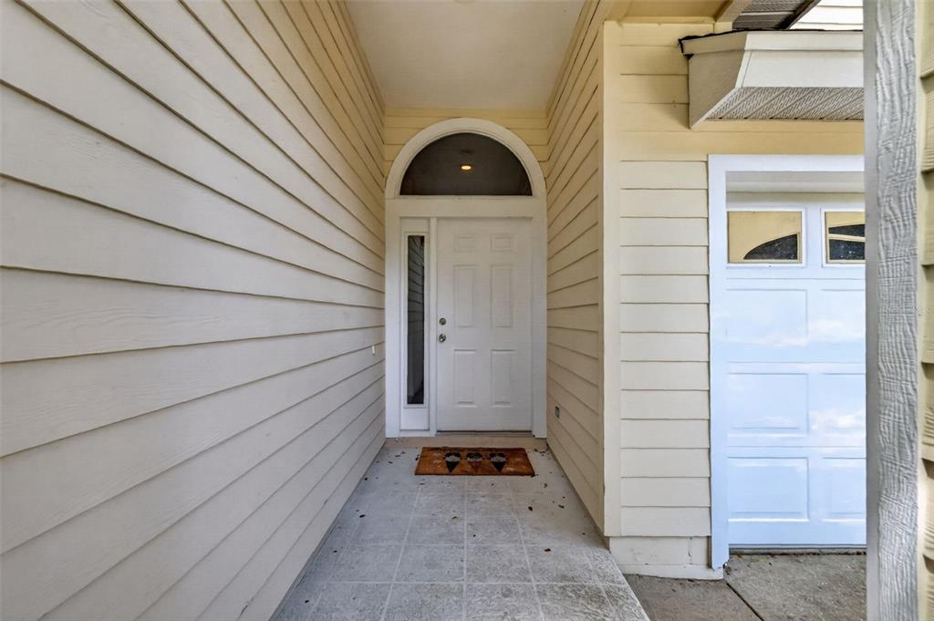 A covered entryway features light-colored horizontal siding, a white front door, and a tiled floor — 10370 SW 51ST LANE, GAINESVILLE, FL