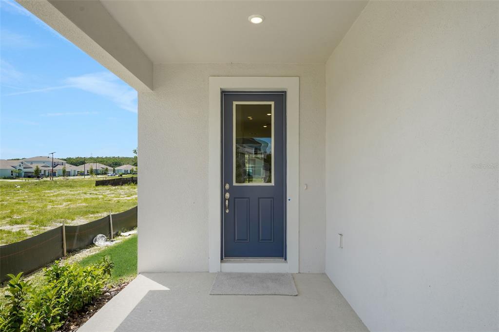 A blue front door with a glass pane opens onto a covered concrete porch — 874 SUNSHOWER DRIVE, LADY LAKE, FL