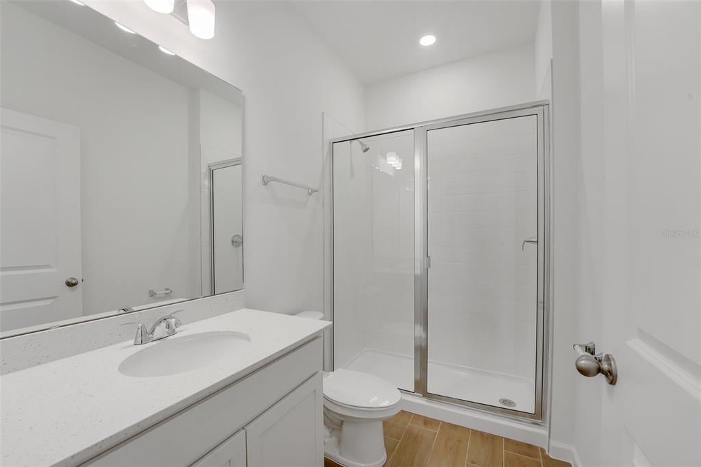 A bathroom features a white vanity, a glass-enclosed shower, and wood-look tile flooring — 874 SUNSHOWER DRIVE, LADY LAKE, FL