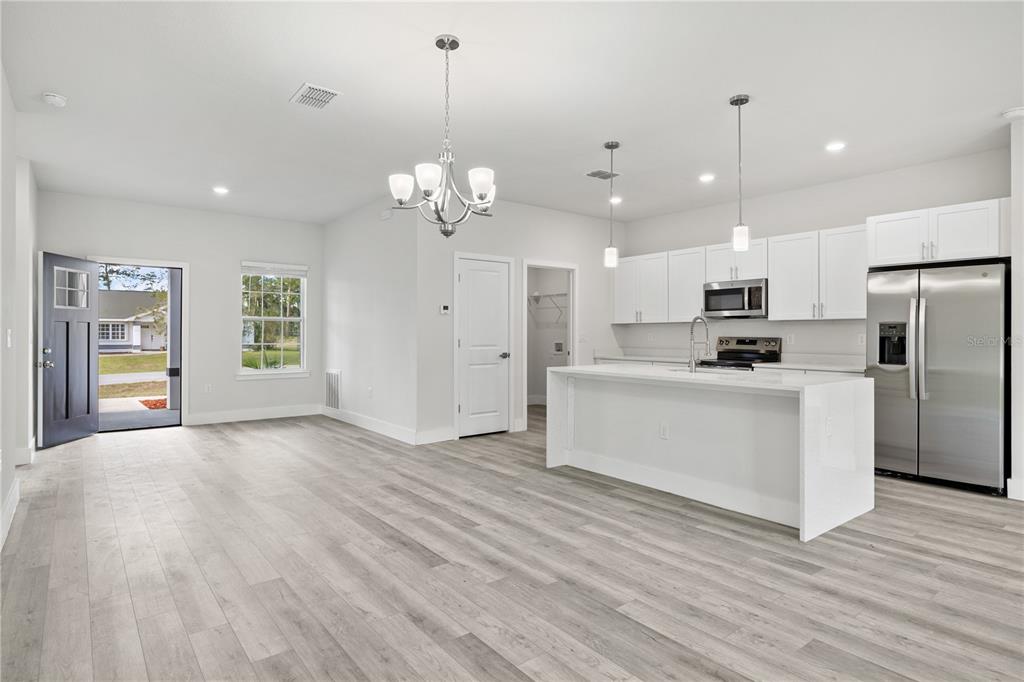 A bright, open-concept kitchen and living area featuring white cabinets, a central island, and flooring — 16616 SW 31ST CIRCLE, OCALA, FL