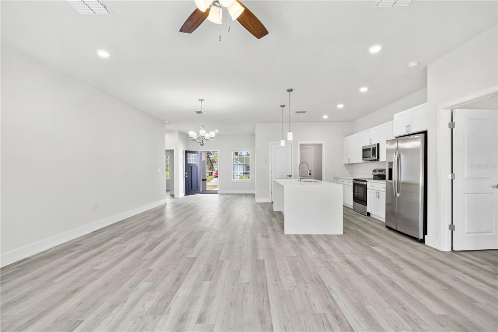 An open-concept kitchen and living area features white cabinetry, stainless steel appliances, and wood-look flooring — 16616 SW 31ST CIRCLE, OCALA, FL
