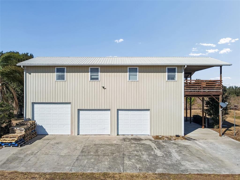 A two-story metal building features three garage doors, four upper-level windows, and a wooden deck — 4026 MCINTOSH ESTATES LANE, PLANT CITY, FL