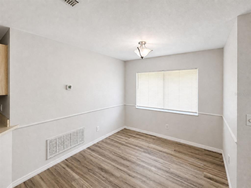 An empty dining area features light-colored walls, wood-look flooring, a window with blinds, and a light — 7904 WATERVIEW WAY, WINTER HAVEN, FL