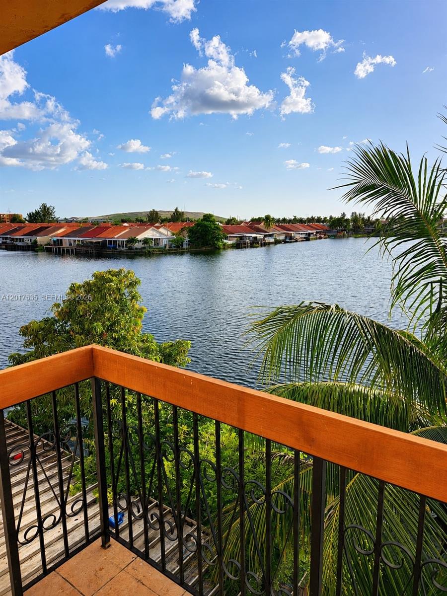 A balcony with a wooden railing overlooks a lake surrounded by houses and palm trees — 5650 W 26th Ct # 207, Hialeah FL 33016, HIALEAH, FL
