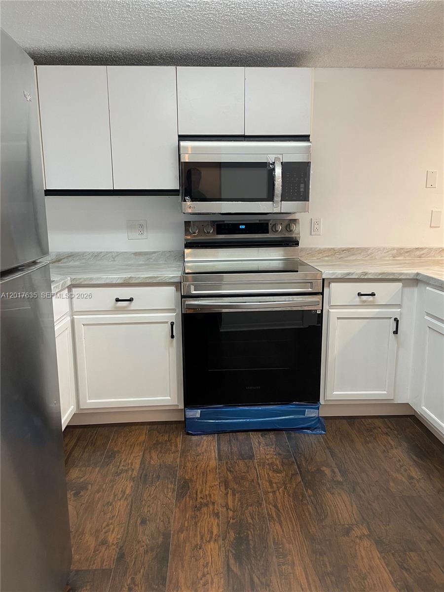 A kitchen features white cabinets, stainless steel appliances, and wood-look flooring — 5650 W 26th Ct # 207, Hialeah FL 33016, HIALEAH, FL