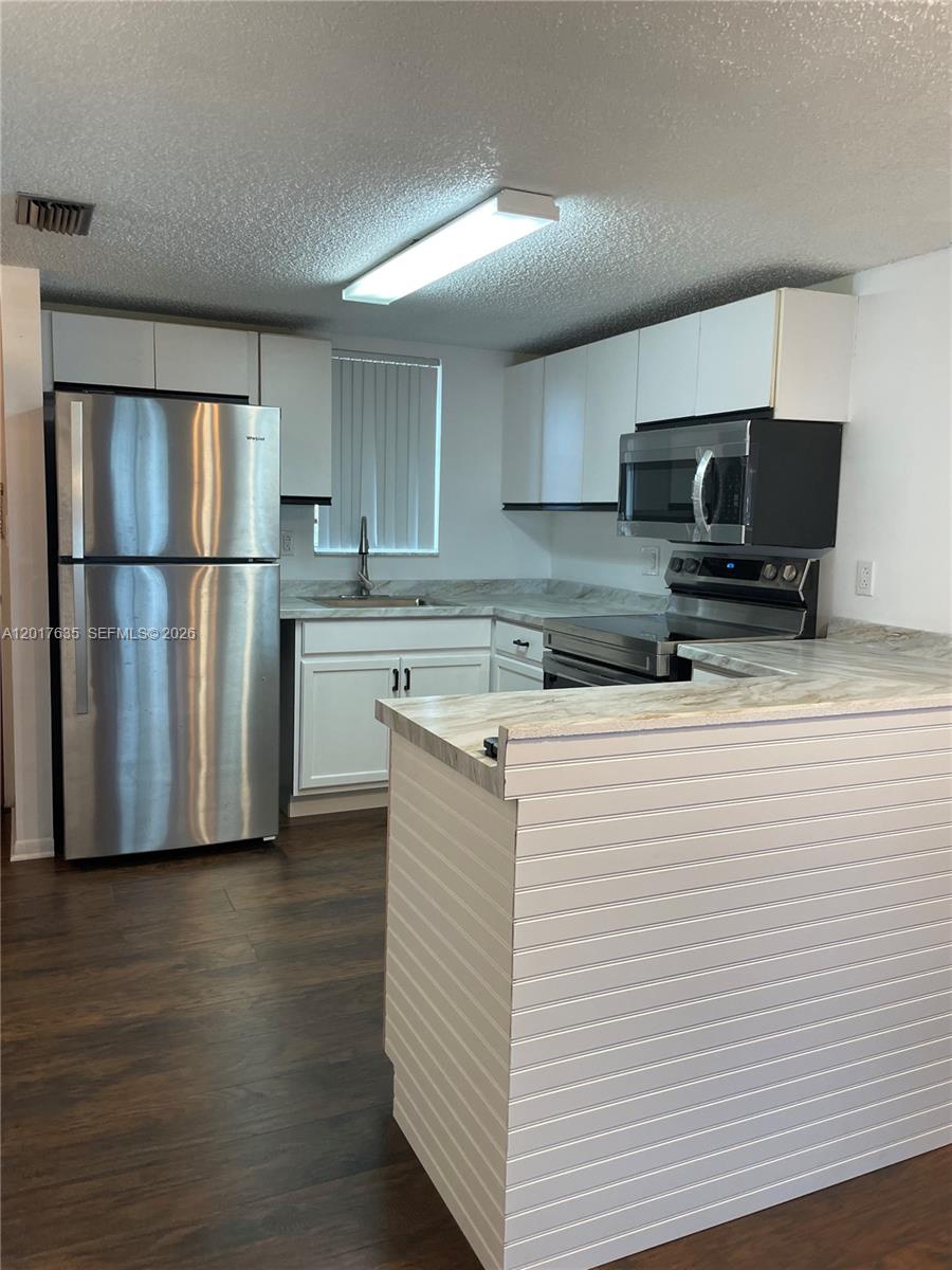 A kitchen features white cabinets, stainless steel appliances, and a peninsula with wood-look flooring — 5650 W 26th Ct # 207, Hialeah FL 33016, HIALEAH, FL