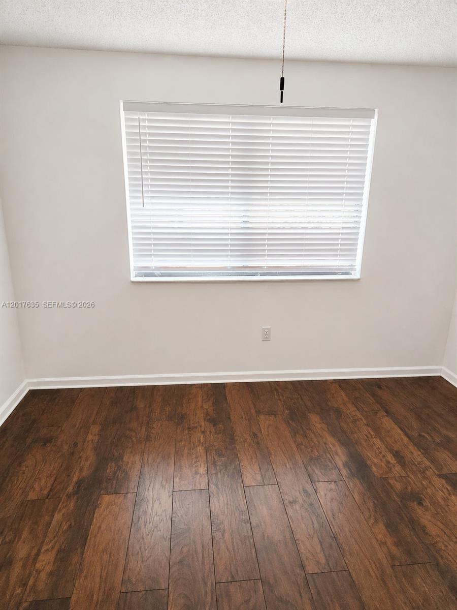 An empty room features white walls, dark wood-look flooring, and a window with blinds — 5650 W 26th Ct # 207, Hialeah FL 33016, HIALEAH, FL