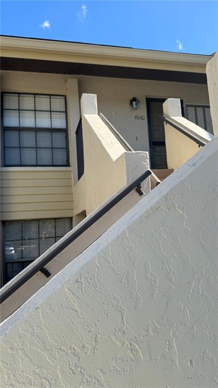 An exterior view of a tan building with a staircase leading to an upper entrance — 4640 WEYBRIDGE UNIT 12, SARASOTA, FL