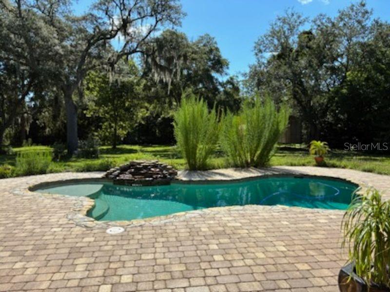 A backyard swimming pool with a stone waterfall feature surrounded by a paver patio — 1521 SHADOW PINES DRIVE, NEW SMYRNA BEACH, FL