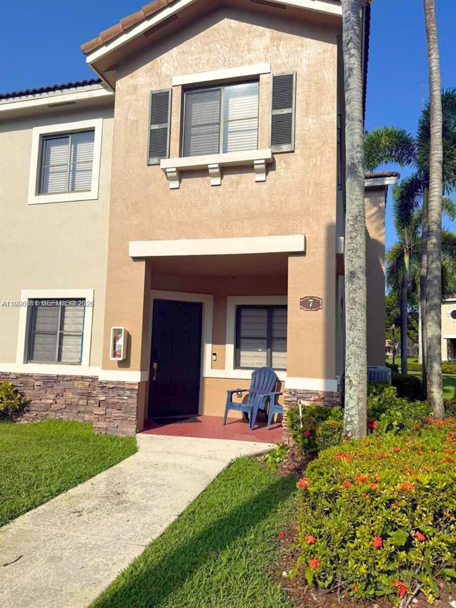 A two-story tan stucco townhouse features a covered entryway, a blue chair, and palm trees — 22711 SW 88th Pl # 23, Cutler Bay FL 33190, CUTLER BAY, FL