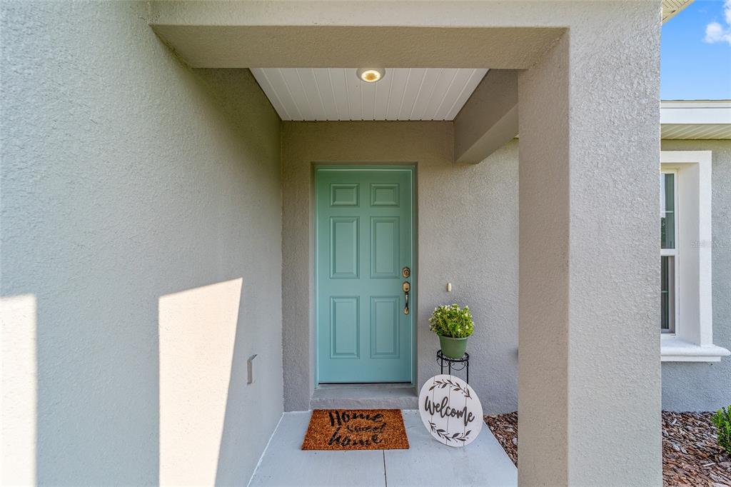 A teal front door is centered under a covered entryway with a welcome sign — 13721 SW 79TH TERRACE ROAD, OCALA, FL