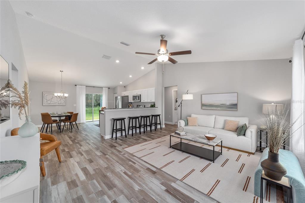 An open-concept living and dining area features vaulted ceilings, wood-look flooring, and a kitchen island — 13721 SW 79TH TERRACE ROAD, OCALA, FL