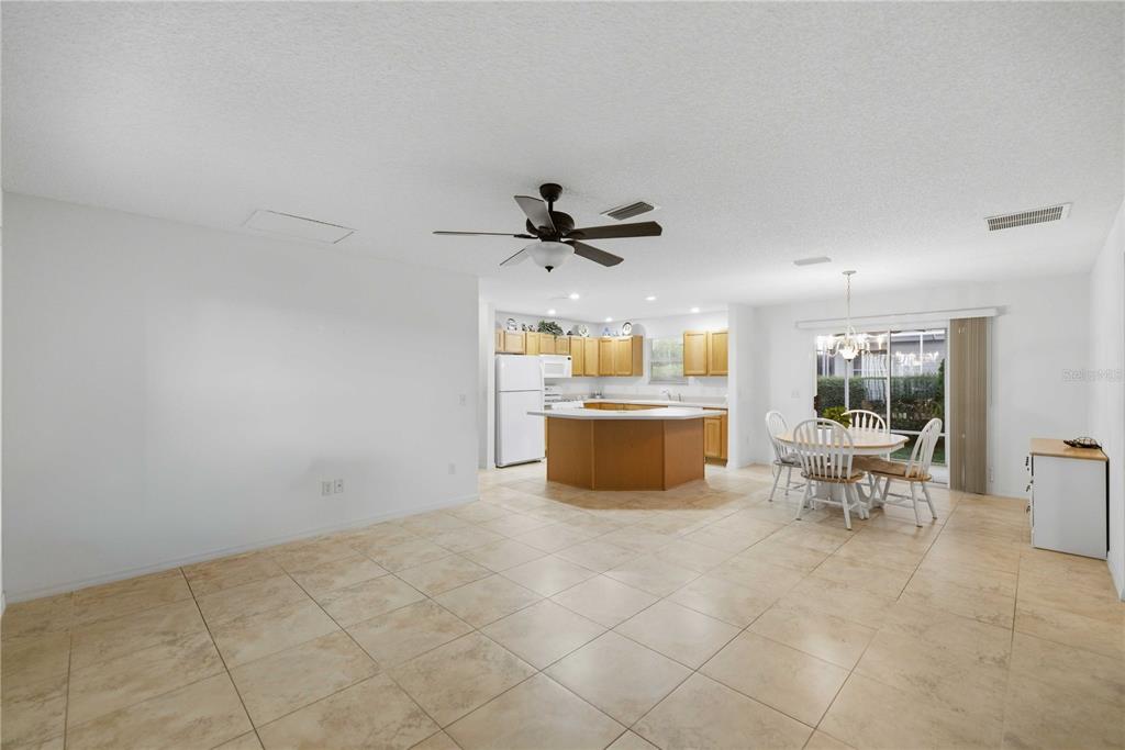 A bright, open-concept kitchen and dining area features light tile flooring and wooden cabinetry — 3431 SIPSEY STREET, THE VILLAGES, FL