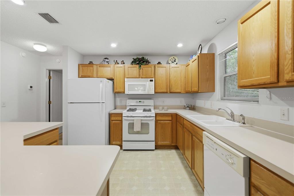 A kitchen features light-colored countertops, white appliances, and oak wood cabinets — 3431 SIPSEY STREET, THE VILLAGES, FL