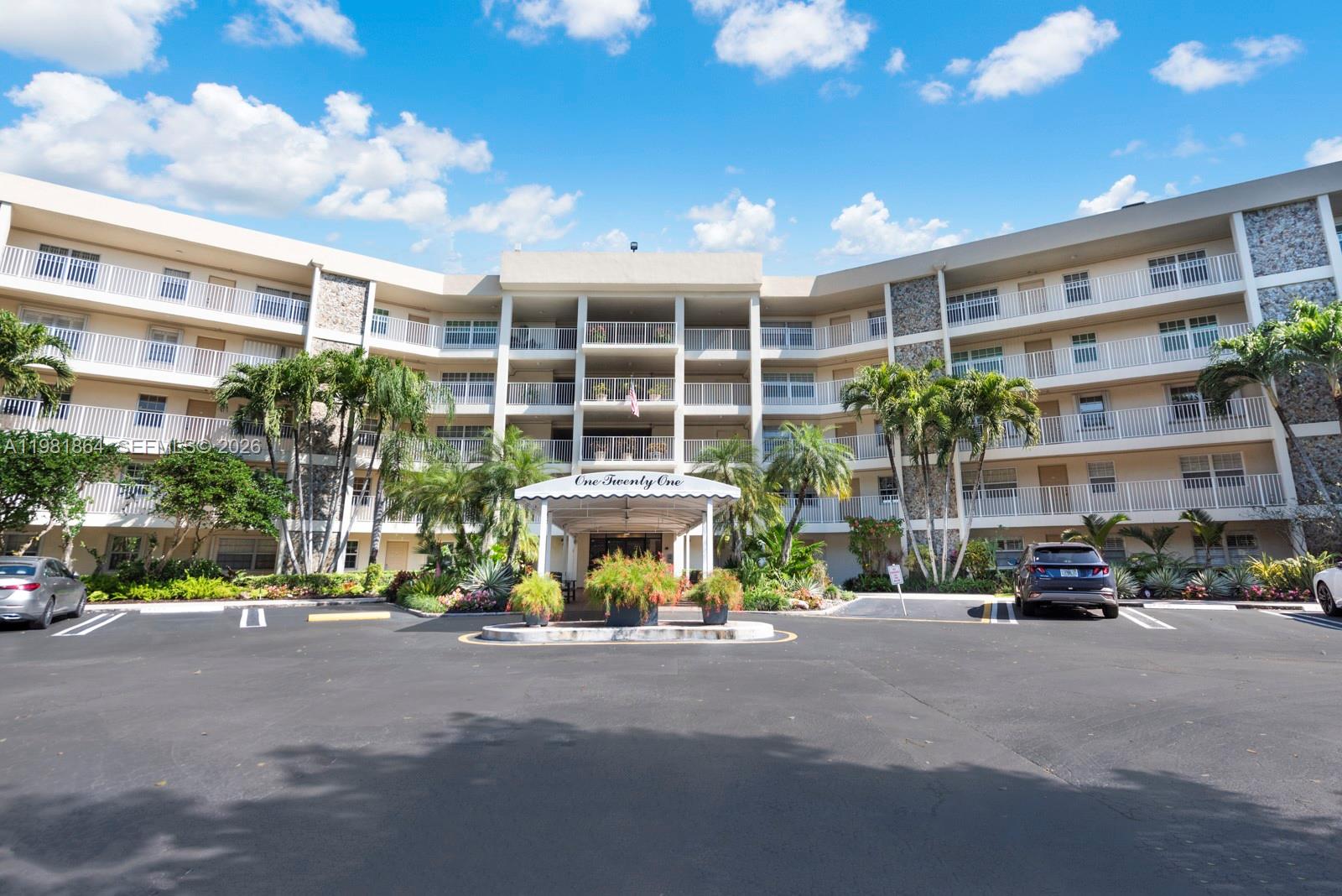 A multi-story apartment building features a central covered entrance and a paved parking lot — 800 Cypress Grove Dr # 509, Pompano Beach FL 33069, POMPANO BEACH, FL