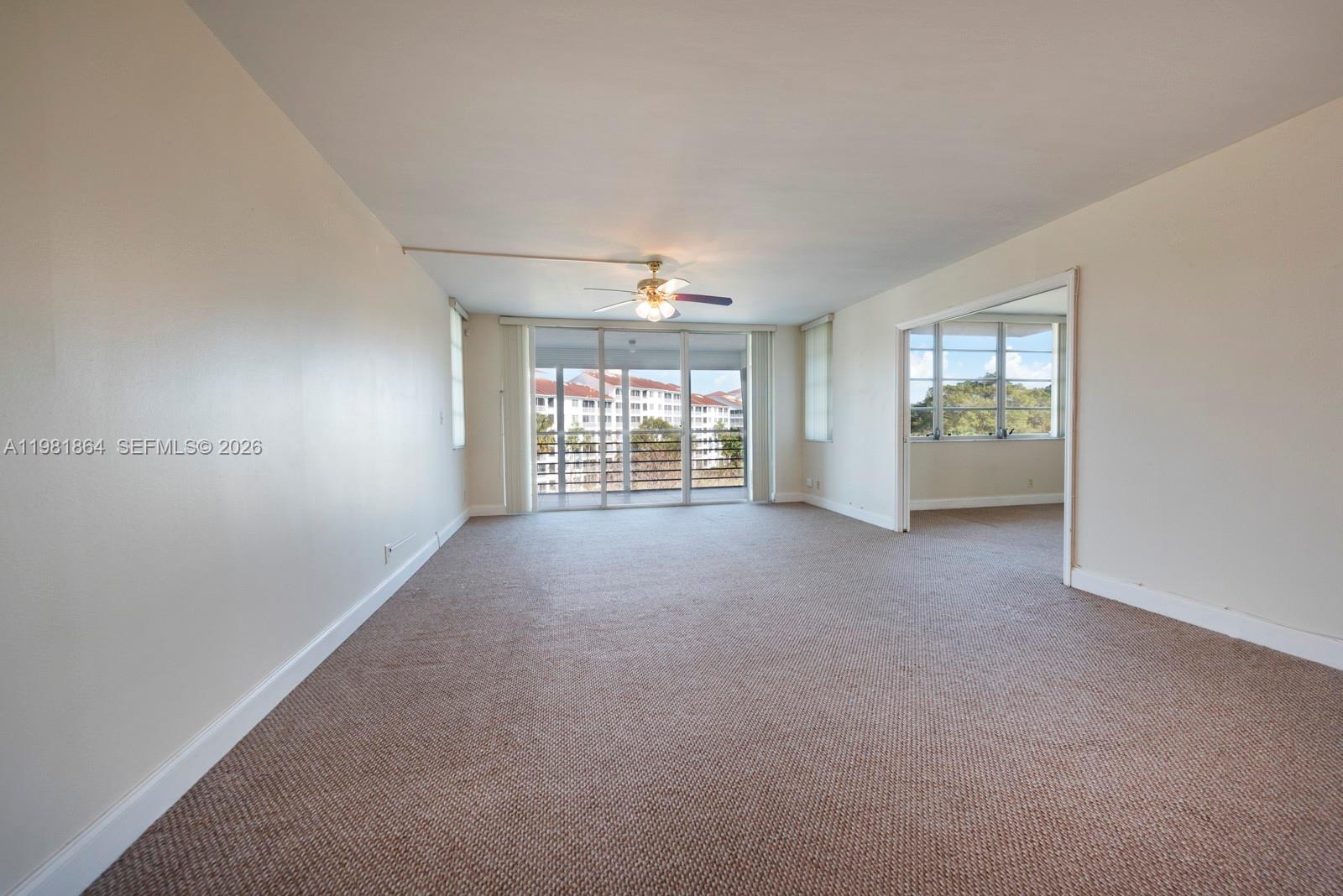 An empty living room features beige carpet, a ceiling fan, and a sliding glass balcony door — 800 Cypress Grove Dr # 509, Pompano Beach FL 33069, POMPANO BEACH, FL