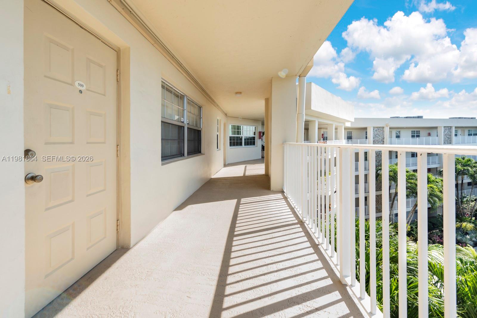 An outdoor apartment building walkway features a white door, beige flooring, and a metal railing — 800 Cypress Grove Dr # 509, Pompano Beach FL 33069, POMPANO BEACH, FL