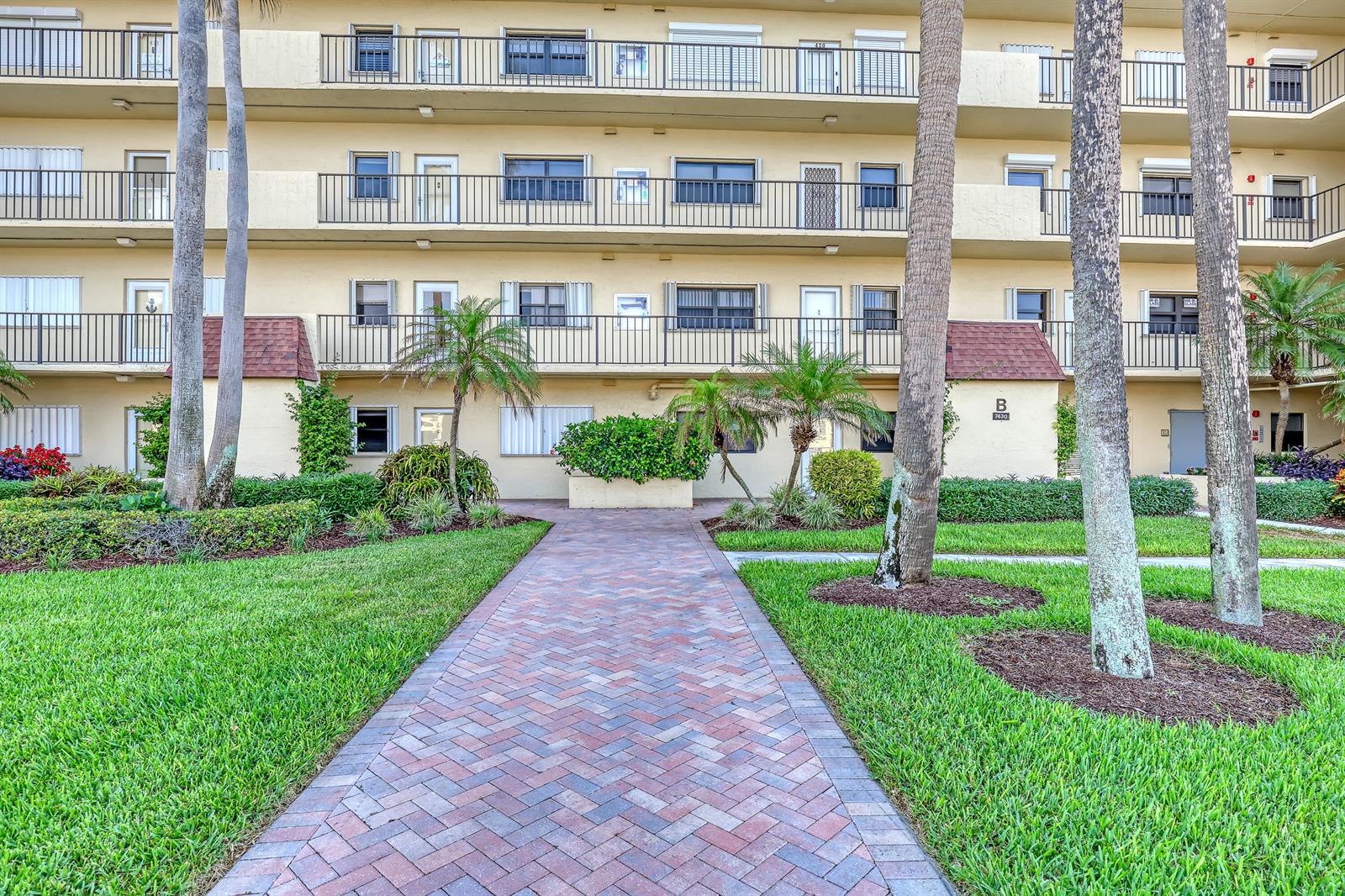A brick walkway leads to the entrance of a multi-story apartment building with palm trees — 7430 S Ocean Drive # 818, Jensen Beach FL 34957, JENSEN BEACH, FL