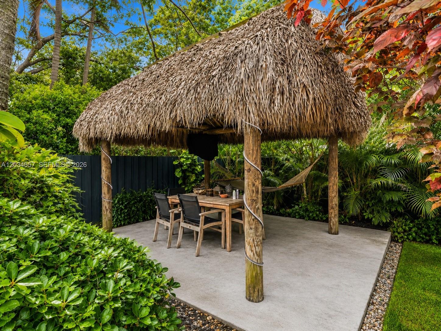 A thatched-roof tiki hut with a dining set and hammock sits on a concrete patio — 1850 Keystone Blvd, North Miami FL 33181, NORTH MIAMI, FL