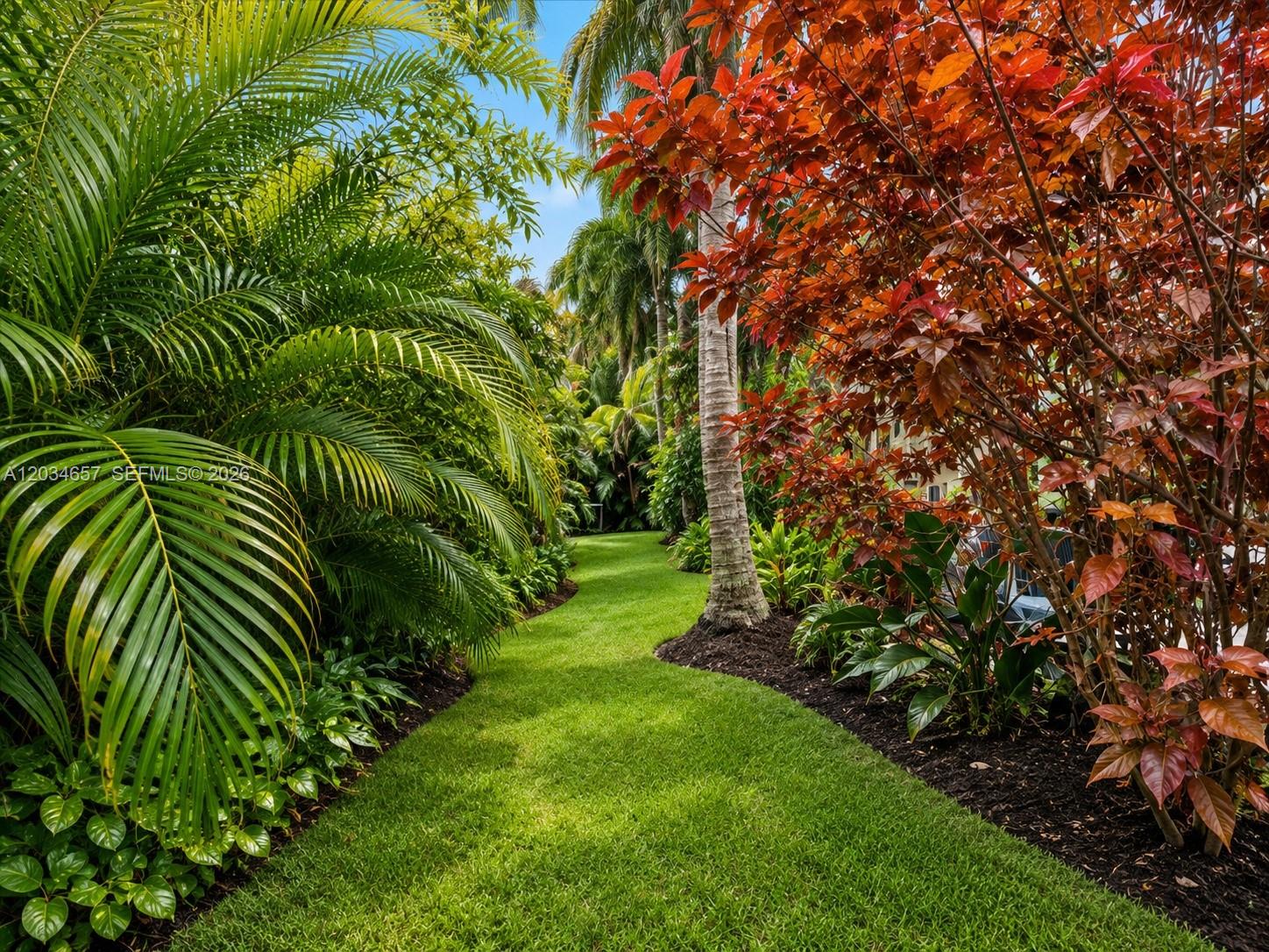 A lush, landscaped garden path winds between palm trees and vibrant red-leafed shrubs — 1850 Keystone Blvd, North Miami FL 33181, NORTH MIAMI, FL