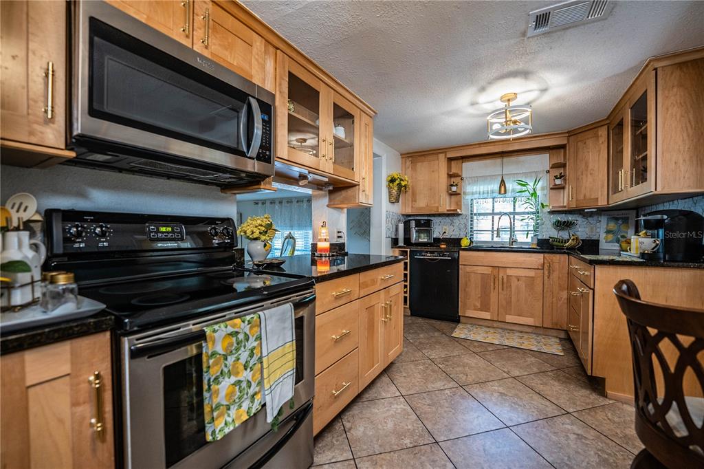 A kitchen features light wood cabinets, black appliances, dark countertops, and tile flooring — 8505 N CAMPBELL ROAD, LAKELAND, FL