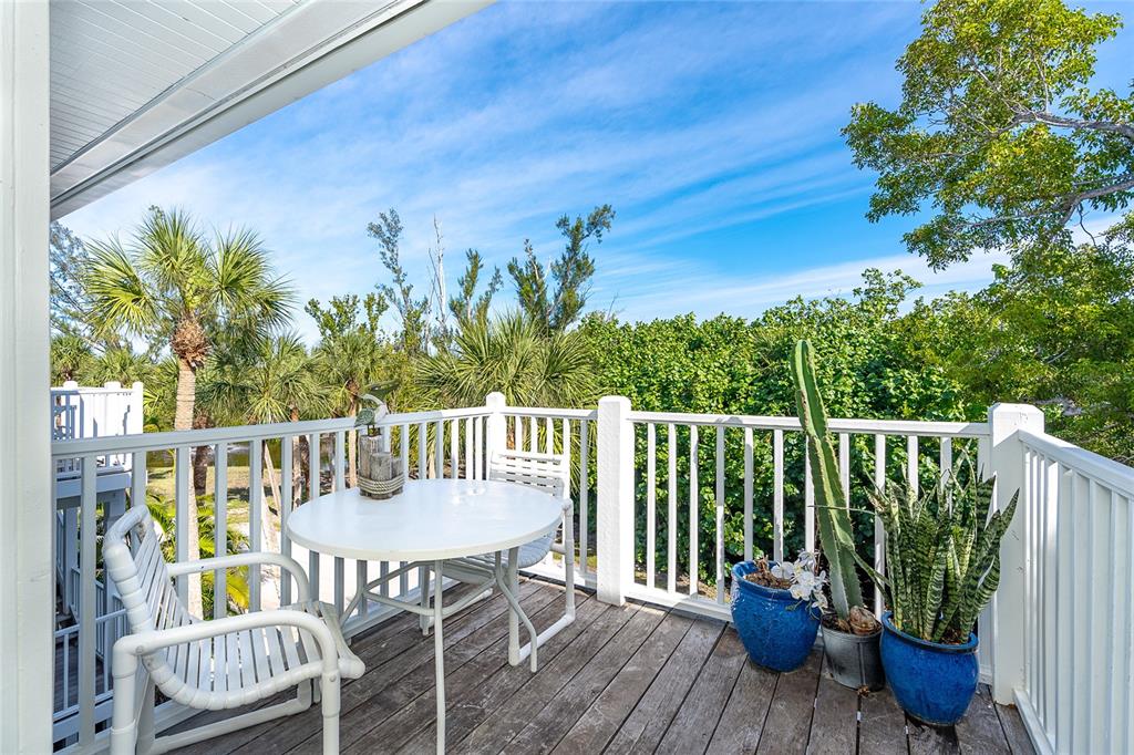 A wooden deck features a white table, two chairs, and potted plants overlooking lush greenery — 7536 PALM ISLAND DRIVE S UNIT 1524, PLACIDA, FL